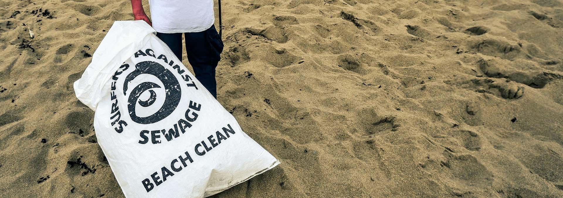 A man with a Surfers Against Sewage Beach Clean bag on a beach